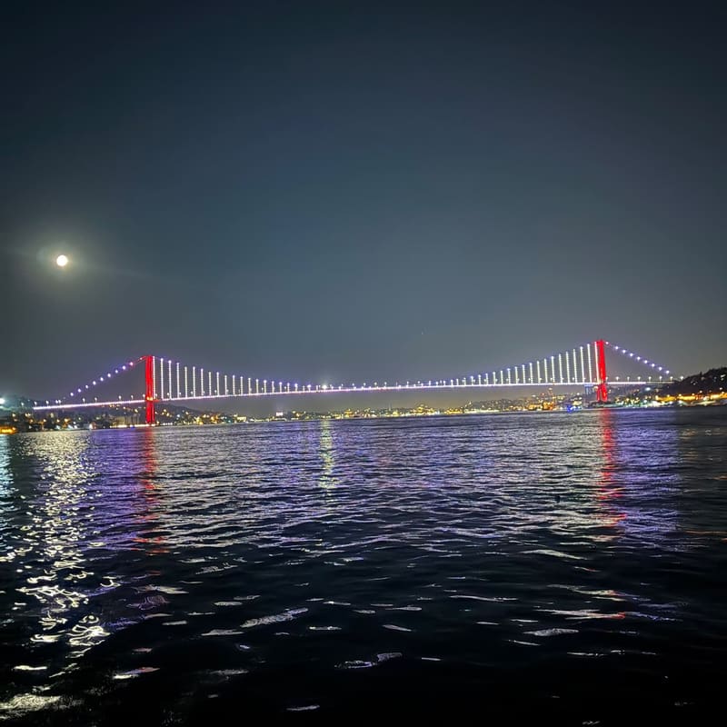 The Bosphorus Bridge in Istanbul lit up at night under a full moon
